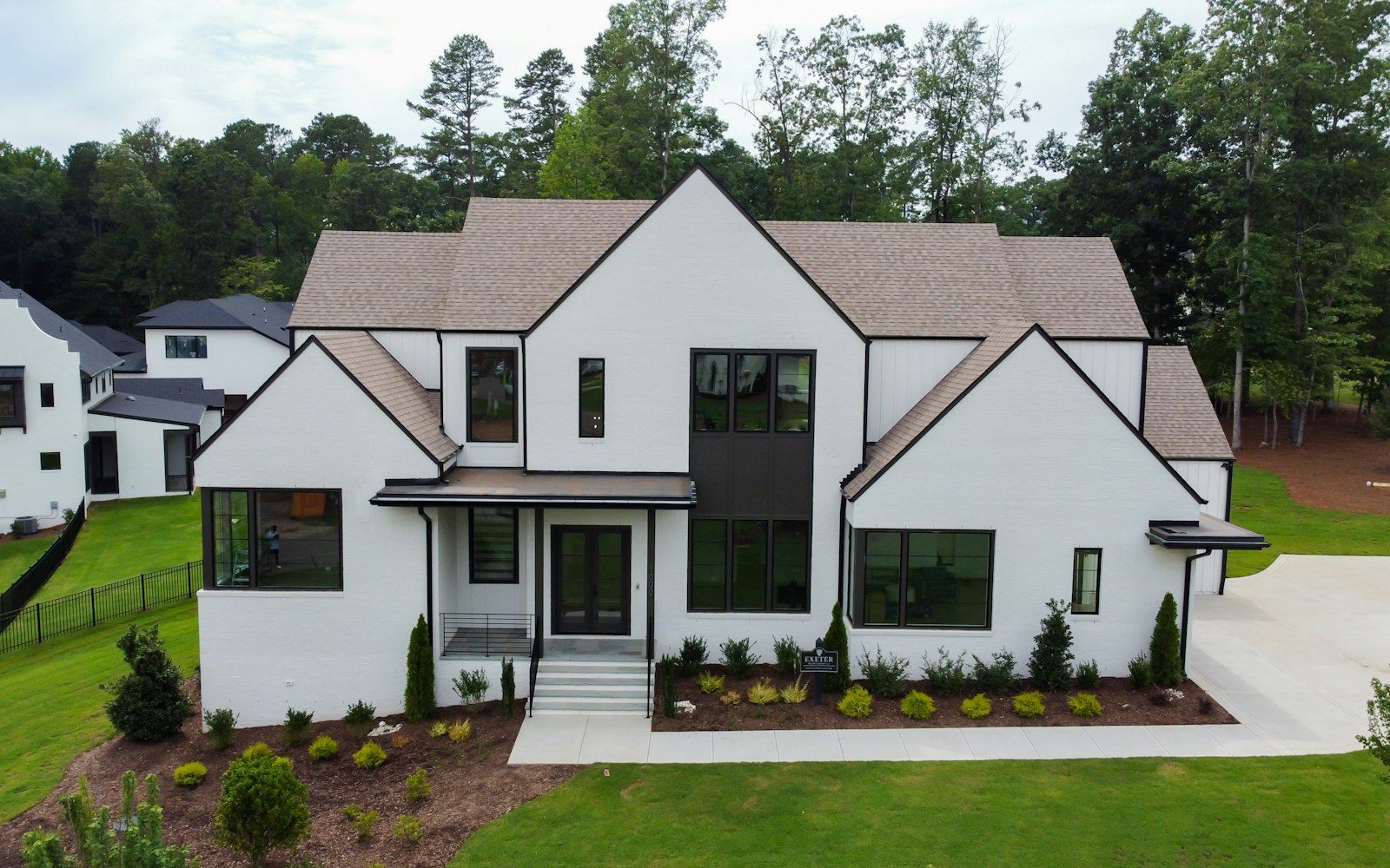 Two-story white modern farmhouse with a dark roof, black-framed windows and a landscaped front yard