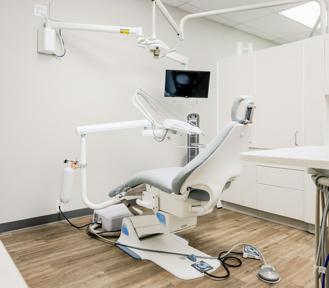 Bright medical treatment room with a patient chair, white cabinetry and wood-look flooring