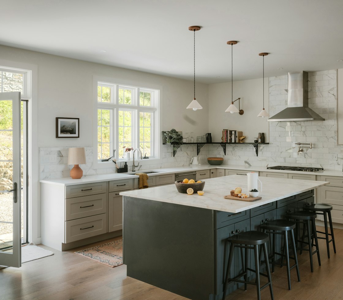 Kitchen with greige shaker cabinets, a dark green island with a marble top, pendant lights and oak floors