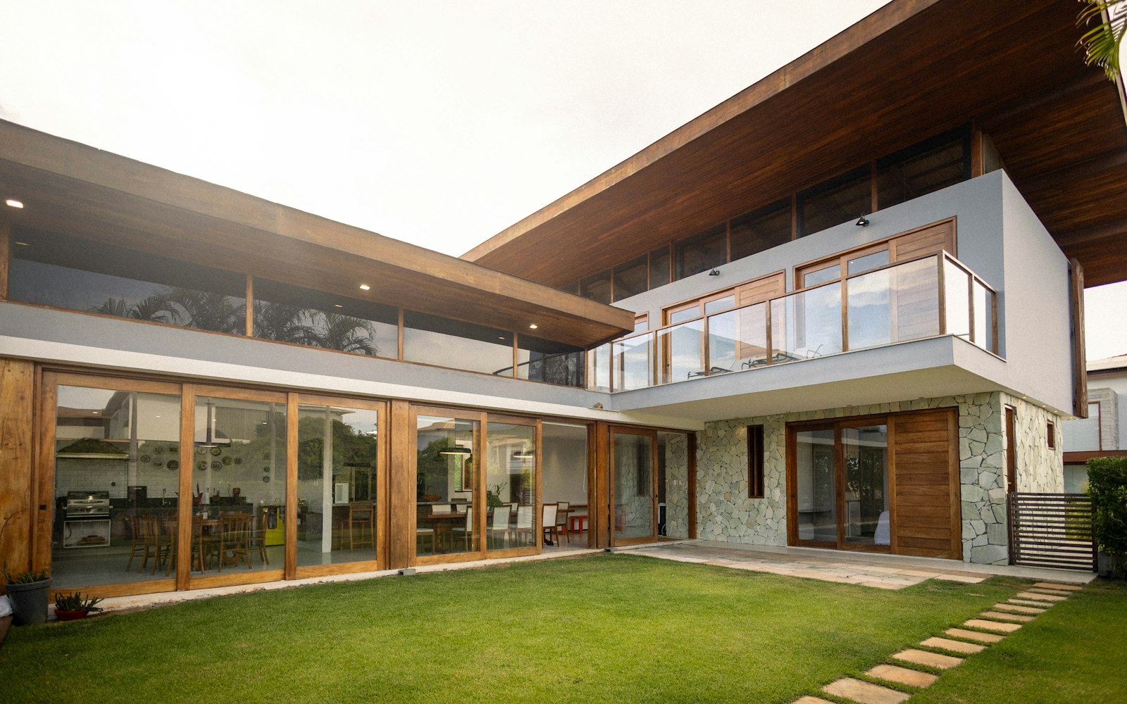 Contemporary two-story home with deep wood eaves, floor-to-ceiling glass, stone walls and a lawn