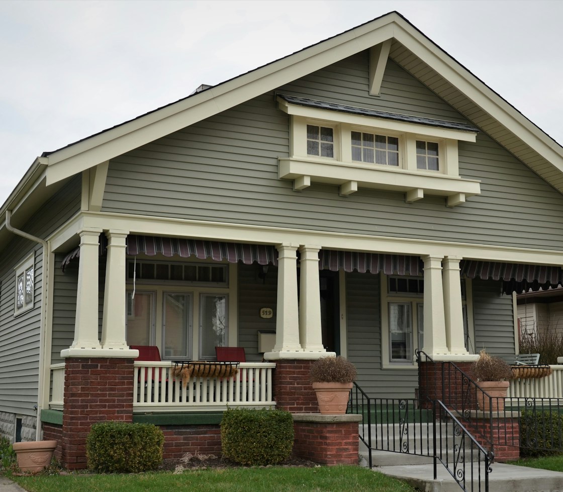 Craftsman bungalow with sage siding, a deep front porch, tapered columns and brick piers